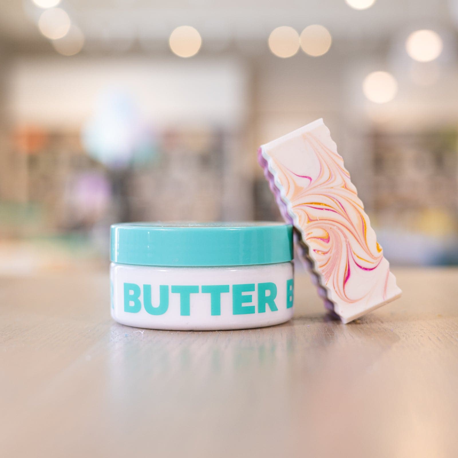 Soap bar with pink and yellow design leaning on body butter container on counter
