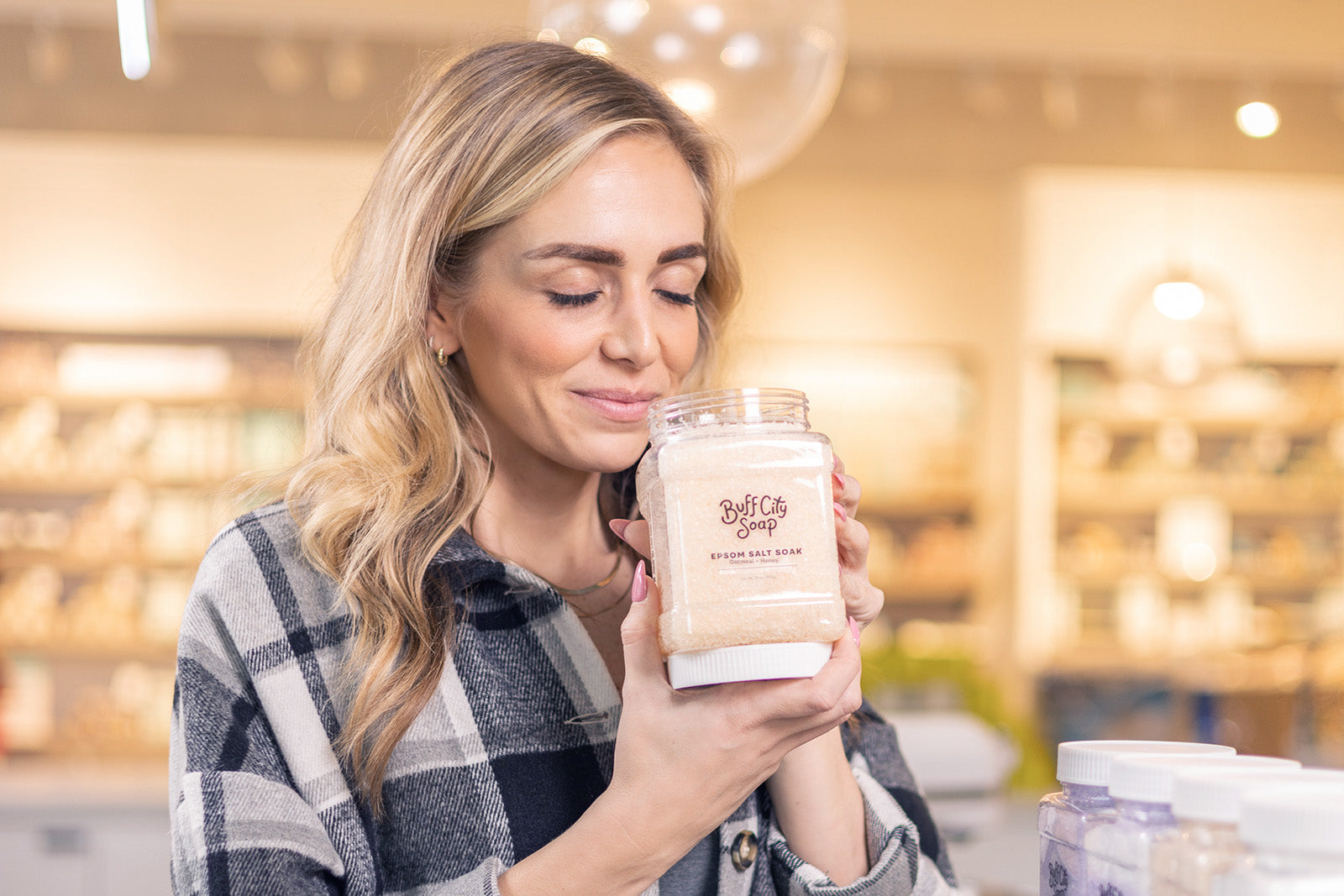 Blonde woman holding Epsom Salt Soak container and smelling inside 