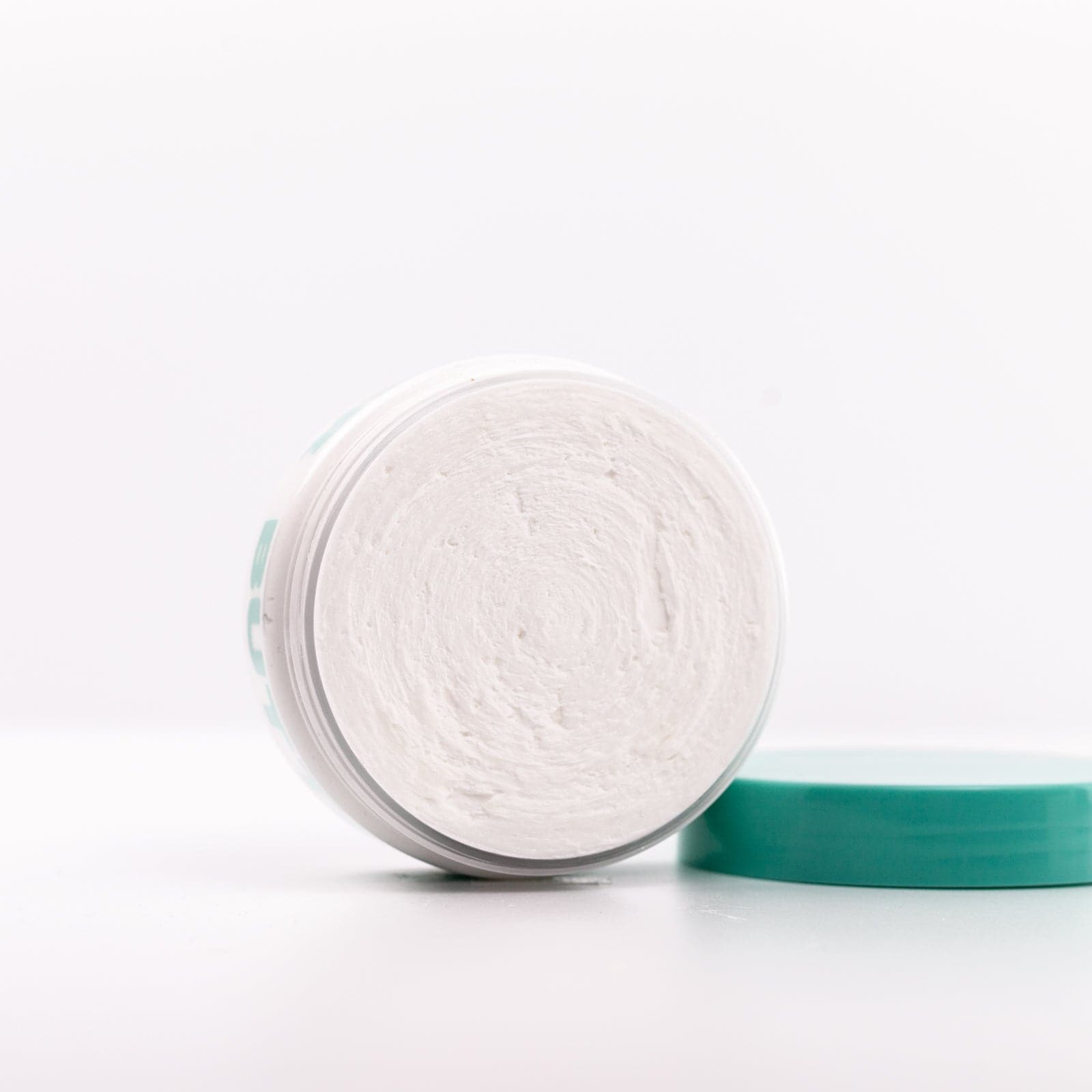 Clear Body Butter container on side with teal lid off in front of white background
