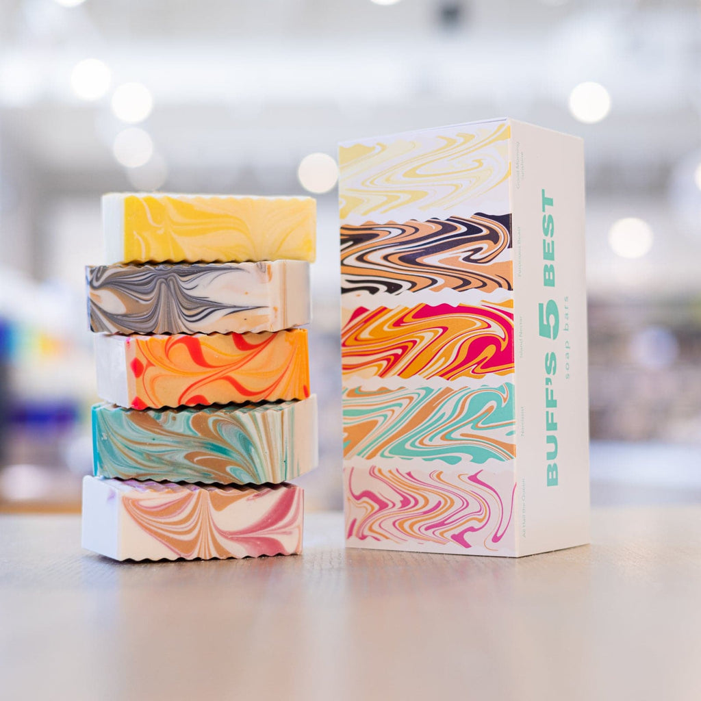 Five multi colored soaps stacked next to soap box 