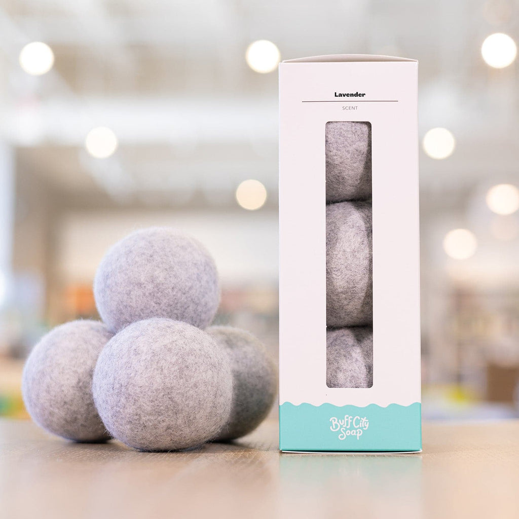 array of grey Buff City Soap's lavender dryer balls next to their box white and teal colored box