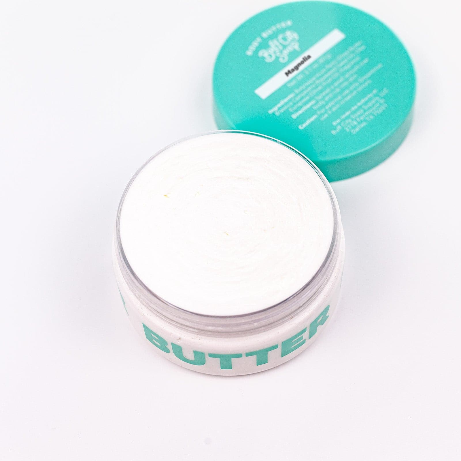 open can of Buff City Soap's magnolia body butter with a teal lid next to it